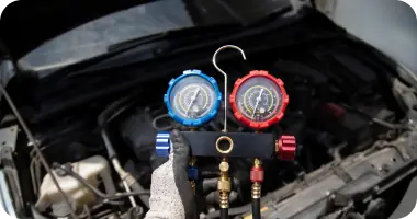 A close-up of a mechanic connecting AC manifold gauges to the air conditioning system in a car's engine bay.