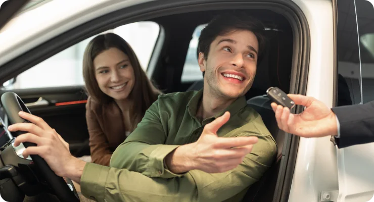 A smiling couple receiving car keys from a salesperson's hand, representing a new car purchase or rental.