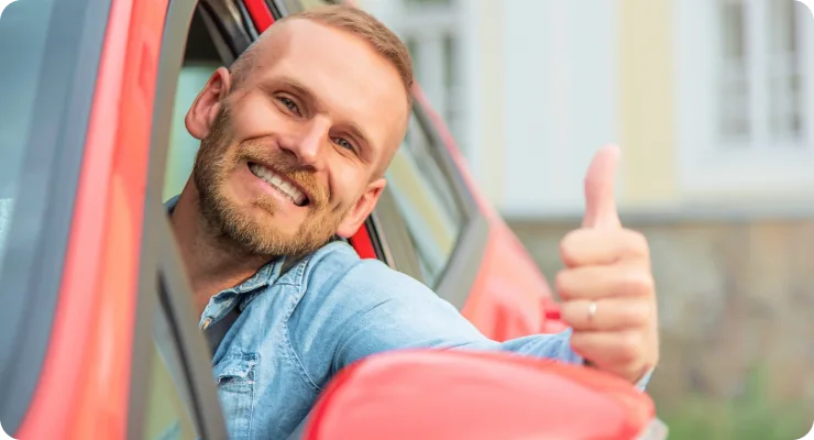 A happy man in the driver's seat of a red car, giving a thumbs-up gesture.