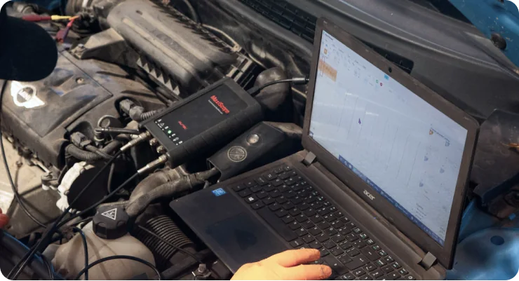 A mechanic using a diagnostic laptop and scanning tool connected to a vehicle's engine bay to read data and troubleshoot a problem.