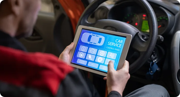 A mechanic or technician using a digital tablet connected to a car's dashboard, displaying diagnostic information.