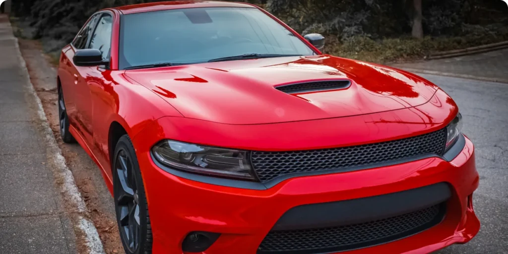 A vibrant red American muscle car, a Dodge Charger, parked on an urban street.