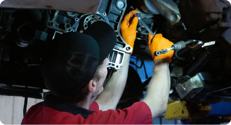 A mechanic with a headlamp working deep within the engine bay, focusing on a component for repair.