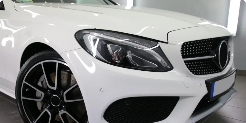 A close-up of the front end of a white Mercedes-Benz luxury car, highlighting its grille and headlight.