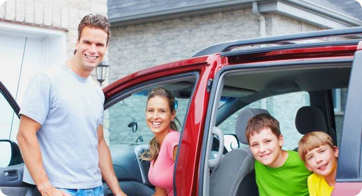 A happy family, a mother, father, and two children, standing next to an open door of a red SUV, smiling.