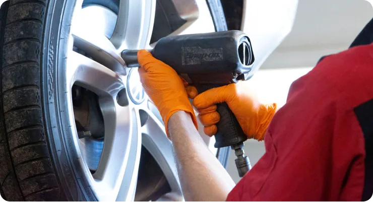 A mechanic using a power tool to work on the lug nuts of a vehicle's tire and wheel.