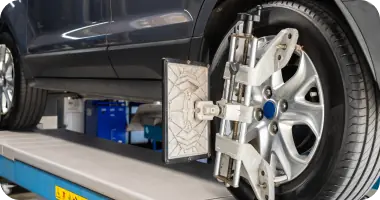 A close-up of a car's rear wheel and tire being measured by a sensor for wheel alignment.