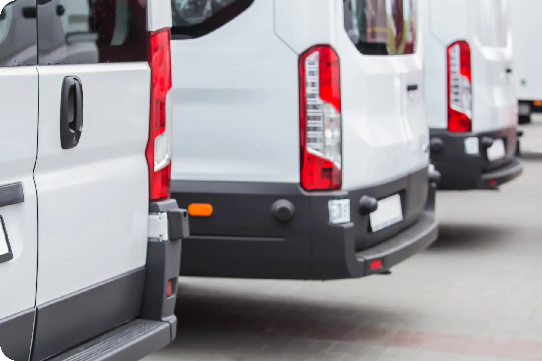 A close-up shot showing the rear of a row of white commercial vans or cargo vehicles parked side-by-side, suggesting fleet service and maintenance.