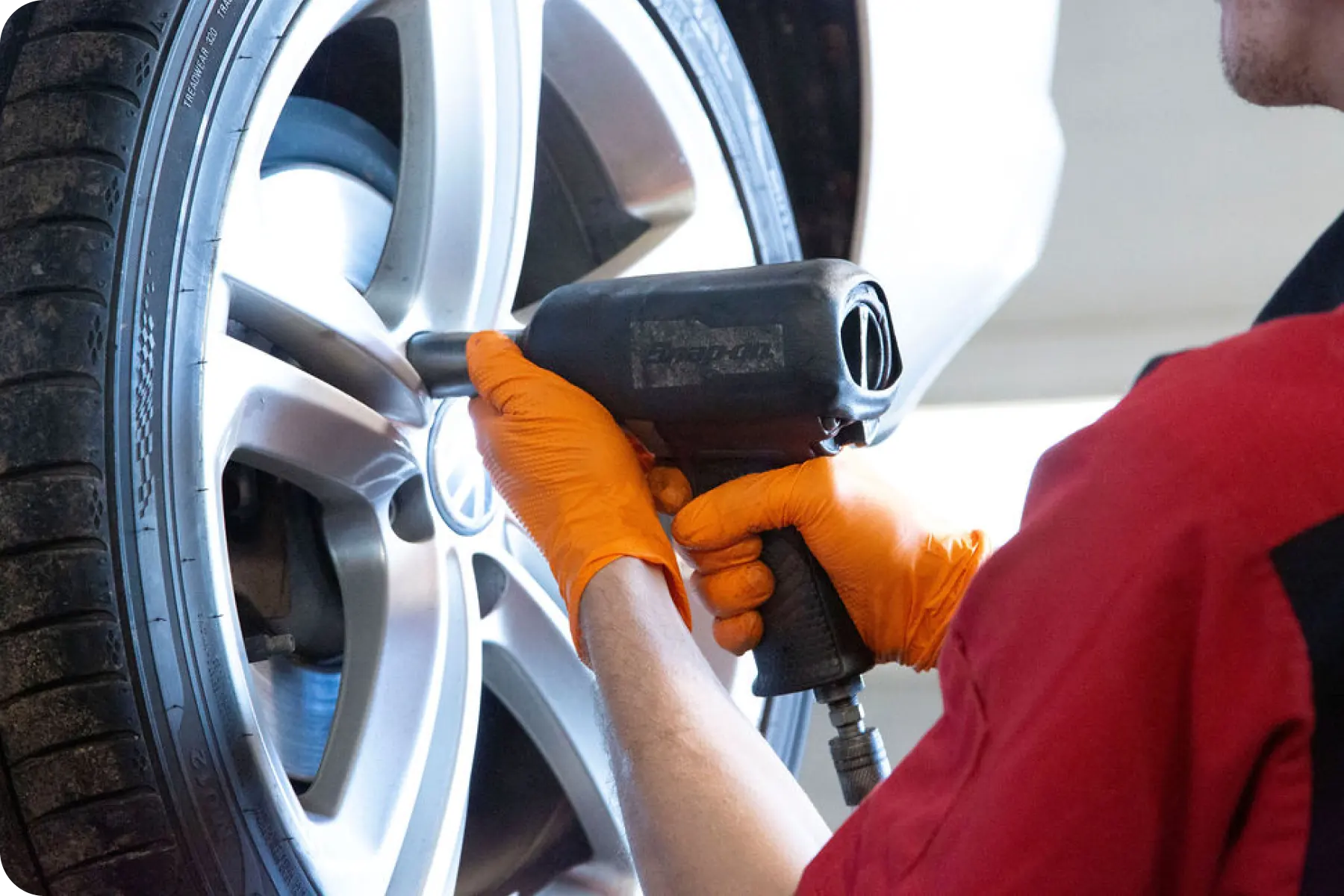 A mechanic using a power tool to work on the lug nuts of a vehicle's tire and wheel.