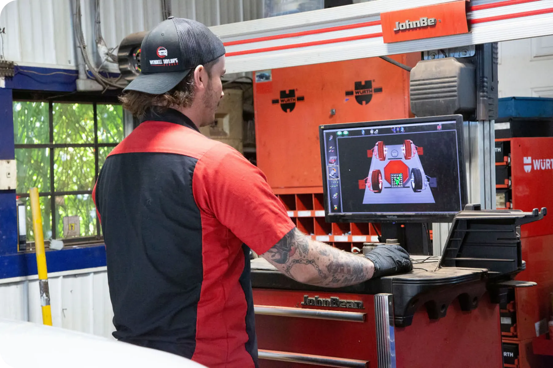 A mechanic seated in a garage, looking at a computer monitor displaying a wheel alignment diagram and data.