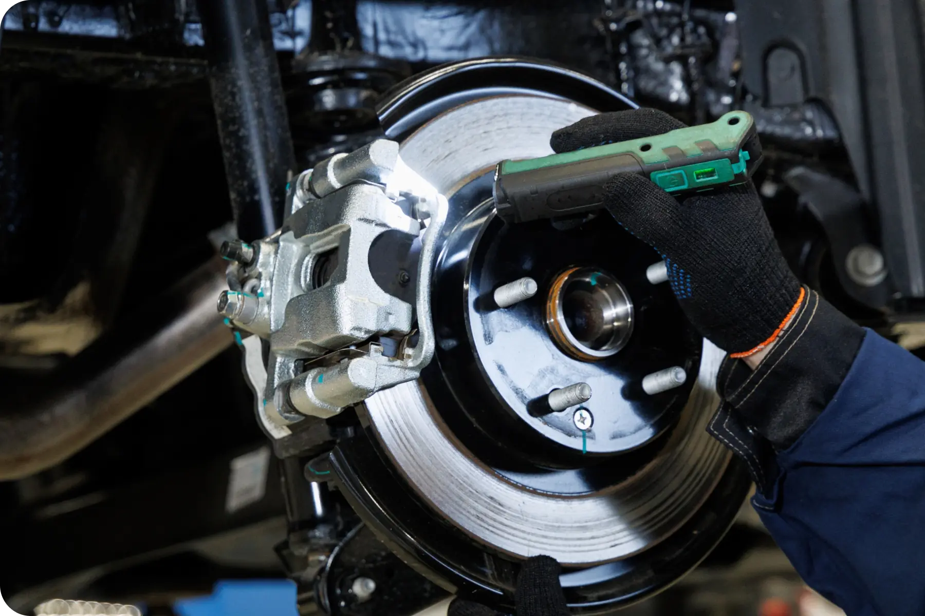 A mechanic wearing gloves installing or adjusting a component on a brake rotor and caliper assembly during a brake service.