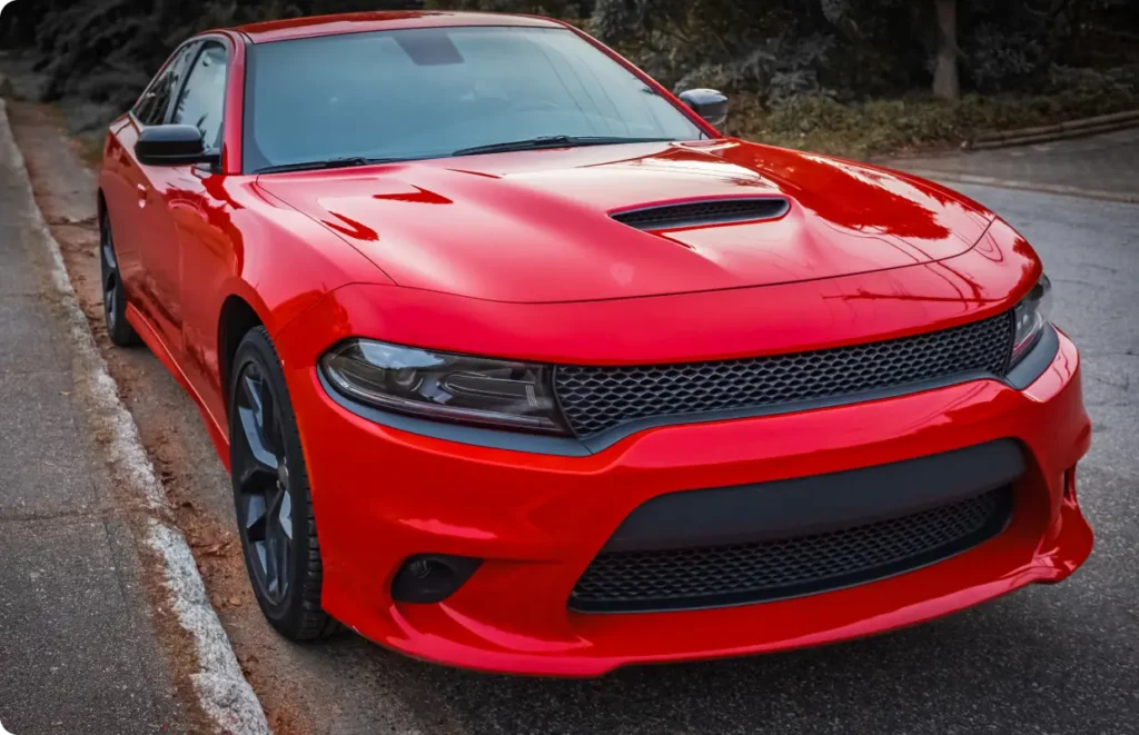 A vibrant red American muscle car, a Dodge Charger, parked on an urban street.