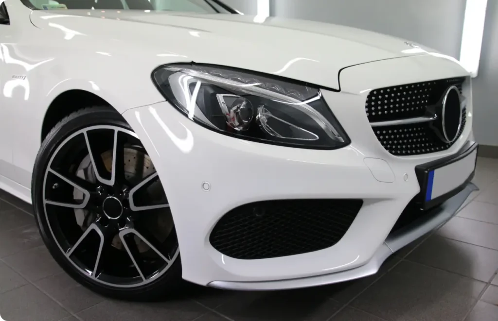 A close-up of the front end of a white Mercedes-Benz luxury car, highlighting its grille and headlight.