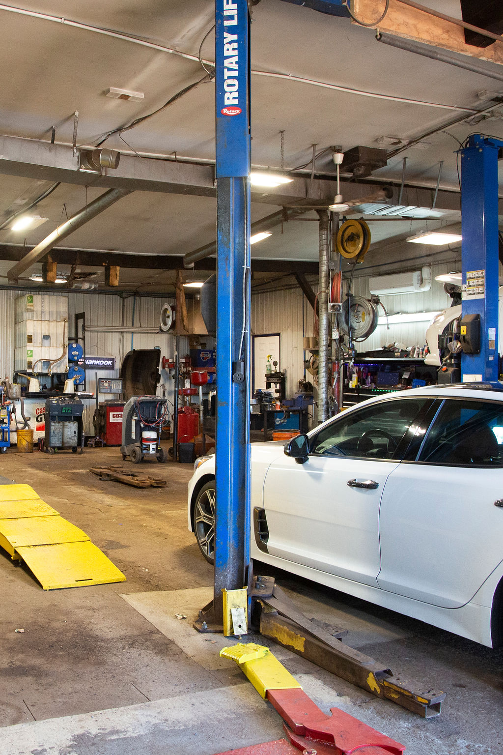 An auto repair bay with a white car parked on an alignment or inspection rack with yellow plates.