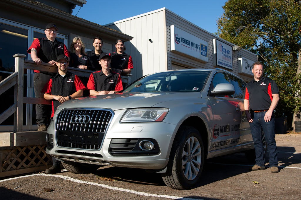 Image of the shop’s team standing beside a silver Audi customer shuttle vehicle in front of the Wendell Taylor’s Garage building, showcasing their professional crew and welcoming facility.