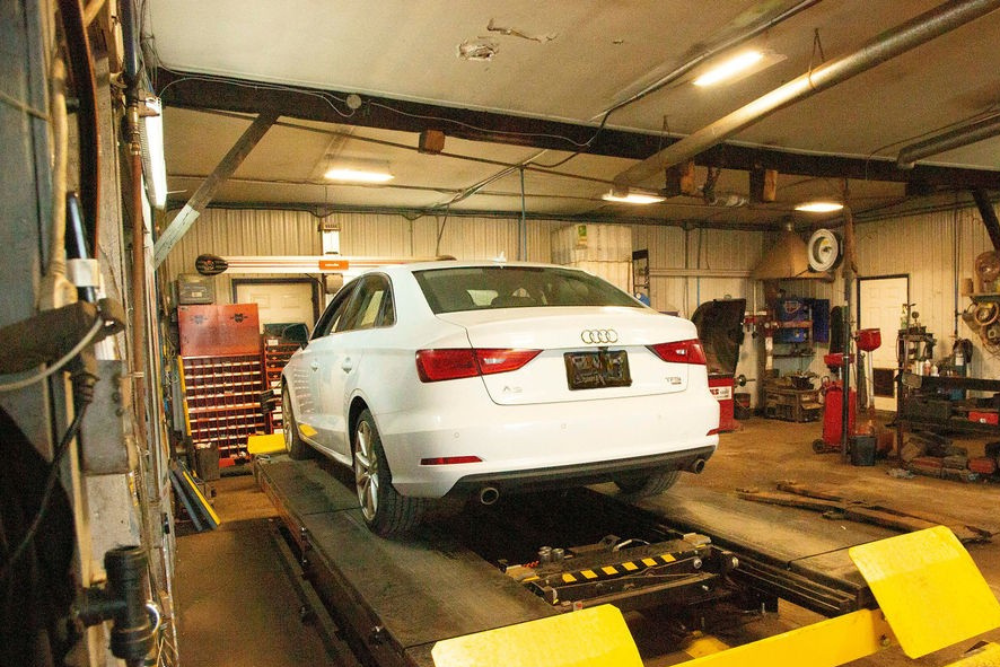 Pre-Purchase Inspection in Stratford, PE At Wendell Taylor's Garage. Image of White Audi sedan on a drive-on service lift inside a repair shop bay